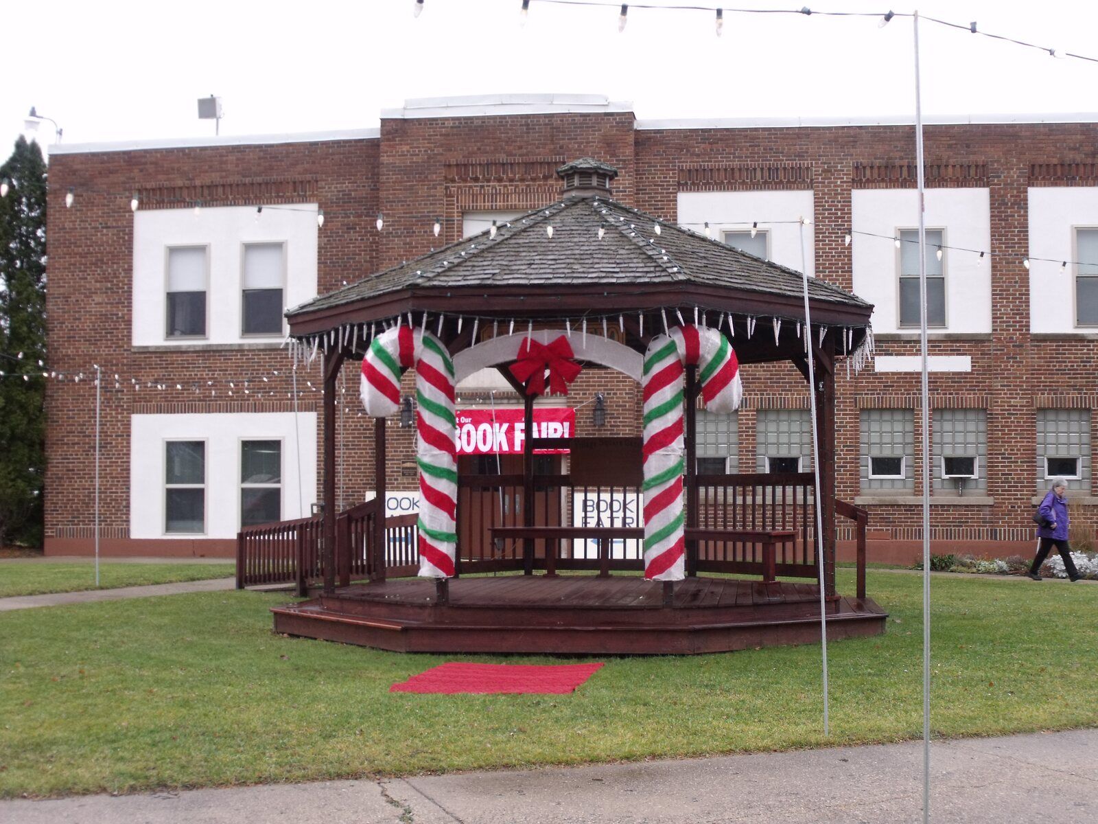 The gazebo on the CRAF Center lawn, its posts wrapped as candy canes, in front of the old brick school
