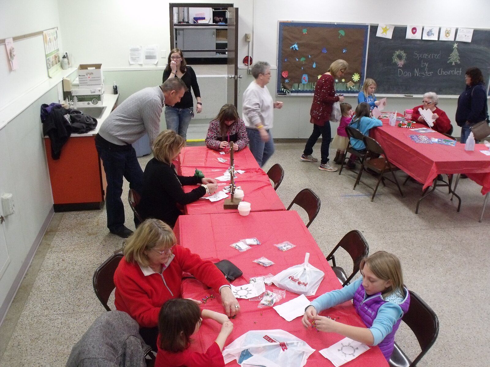 Children and volunteers make Christmas crafts at long red tables in the Kids' Corner