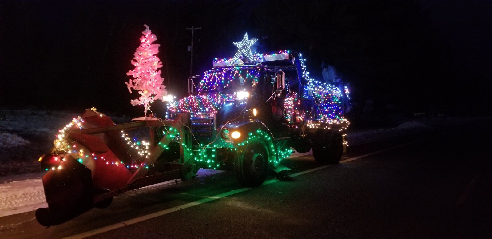 A tractor and float wrapped in blue, green and pink lights, with a lighted tree and star