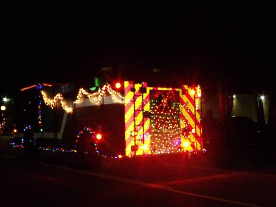 A fire truck covered in Christmas lights rolls down Lake Street at night