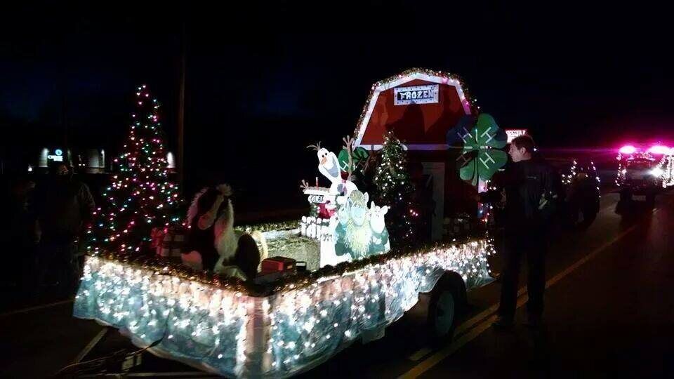 A float trimmed in white lights, with a lighted tree and a red barn, in the Electric Light Parade